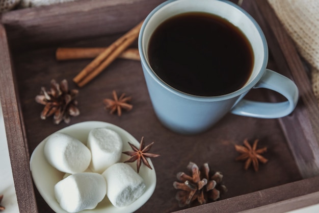 Taza de café en bandeja de madera rústica con malvavisco dulce, piñas y palitos de canela