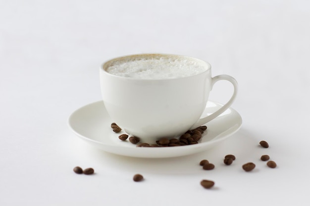 Taza de café blanca con plato y granos de café aislados en fondo blanco. Buenos días.