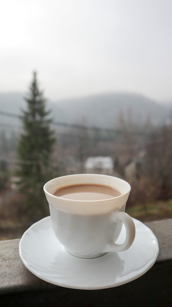 Taza de café blanca sobre fondo de naturaleza abstracta. Una taza de café en el balcón con vista a la naturaleza detrás. Taza de cerámica con una bebida en el balcón del hotel.