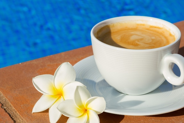 Taza de café blanco en el borde de la piscina