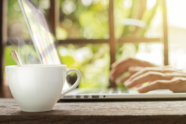 Taza de café blanco caliente con laptop de trabajo empresario fondo de jardín verde