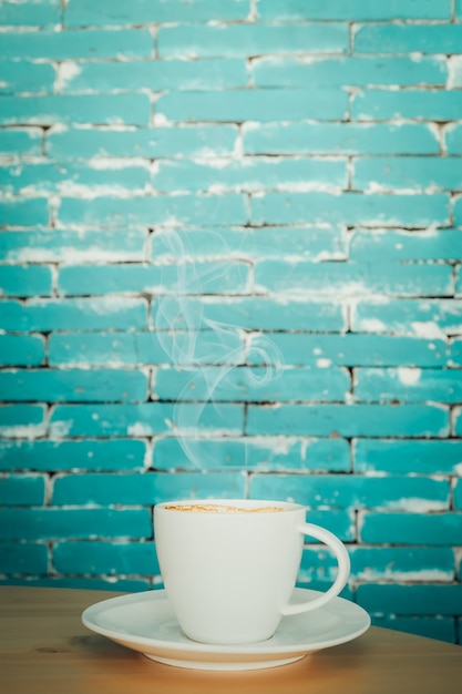 Taza de café blanco caliente en la mesa de madera sobre fondo verde