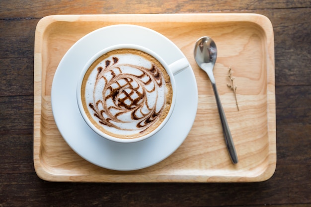 Taza de café blanco con hermoso patrón de arte en la cuchara de madera whute bandeja en la mesa. Seleccionar enfoque