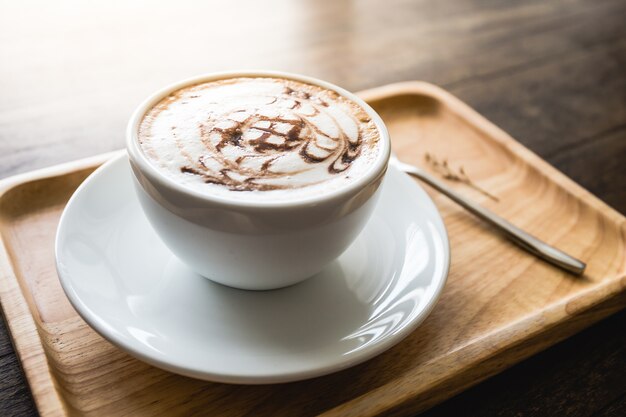 Taza de café blanco con hermoso patrón de arte en la cuchara de madera whute bandeja en la mesa. Seleccionar enfoque