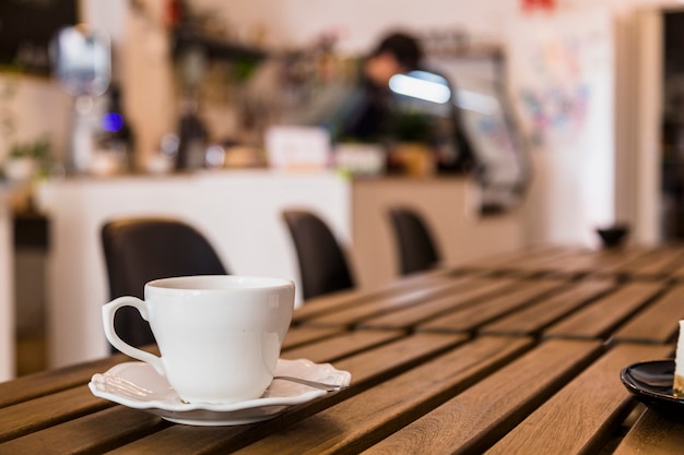 Foto taza de café blanco y platillo sobre la mesa de madera en la barra de café