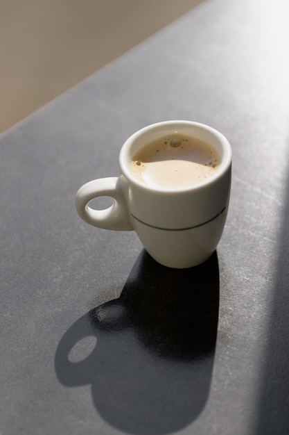 Una taza de café blanco con sombras duras en el fondo de la mesa gris. Concepto de café de la mañana
