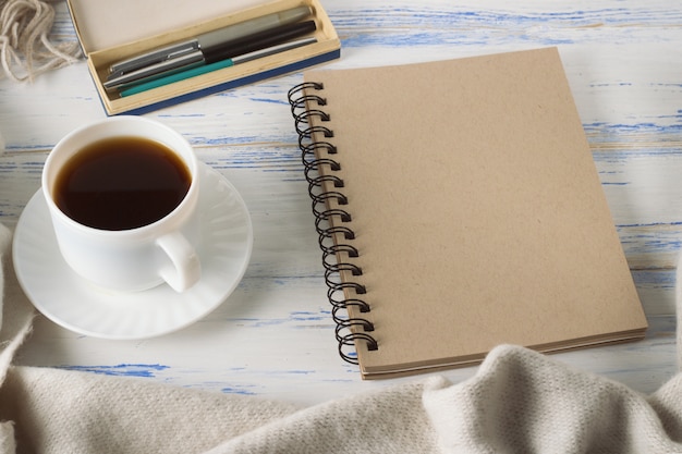 Taza con café, Bloc de notas, bolígrafos en la vieja mesa de madera blanca. Concepto de primavera