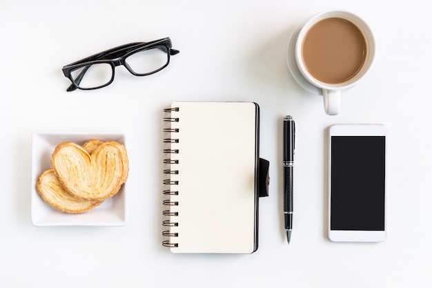 Taza de café con bocadillos, teléfono móvil y notebook en la oficina de escritorio con espacio de copia, vista superior