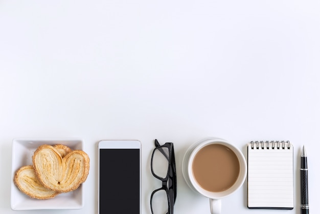 Taza de café con bocadillos, teléfono móvil y notebook en la oficina de escritorio con espacio de copia