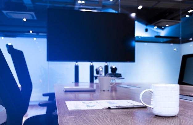 Taza de café bolígrafo y papeleo en la mesa con fondo de televisión de pantalla en blanco en la reunión