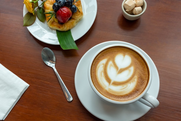 Taza de café y bollo danés con bayas en mesa de madera.