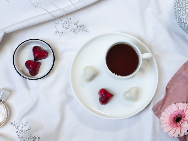Taza de café, bombones y flores en ropa de cama blanca y limpia. Día de San Valentín