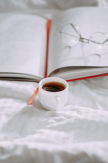 taza de café y booka taza de café un libro y vasos redondos en el fondo de una cama blanca l