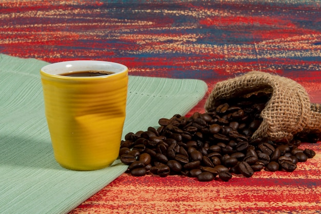 Taza de café brasileño junto a la bolsa con granos tostados cayendo en una mesa oxidada