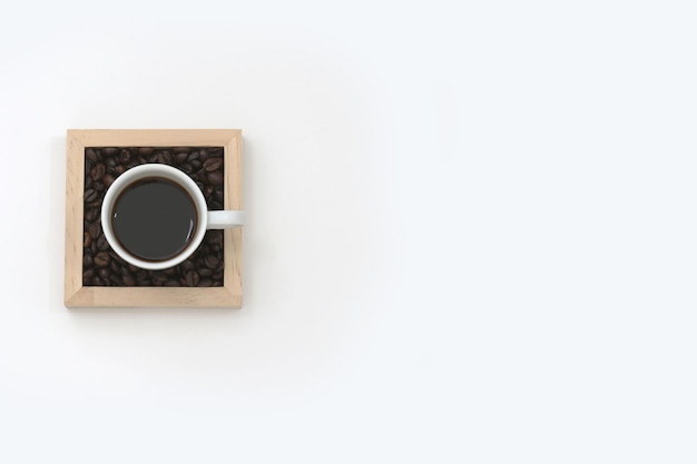 Una taza de café en una caja de madera con frijoles negros sobre un fondo blanco.