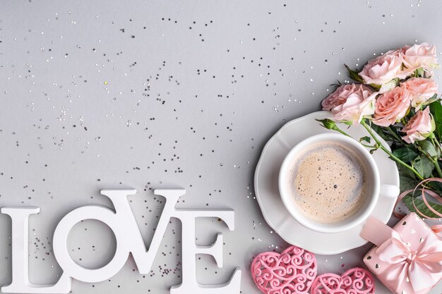 Taza de café, caja con regalo y rosas rosadas sobre un gris festivo