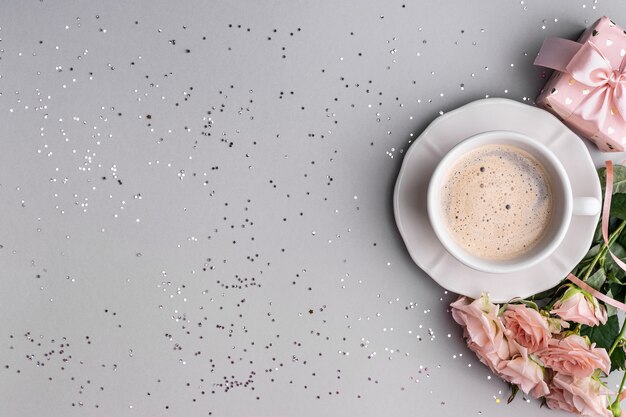 Taza de café, caja con un regalo y rosas rosadas sobre una superficie gris festiva