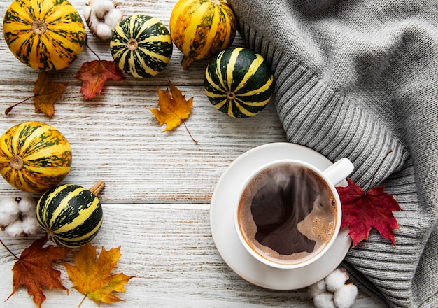 Taza de café, calabazas y hojas secas.