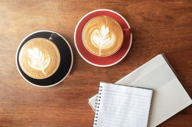 Foto taza de café caliente con arte del latte en forma de hoja y libro vacío.