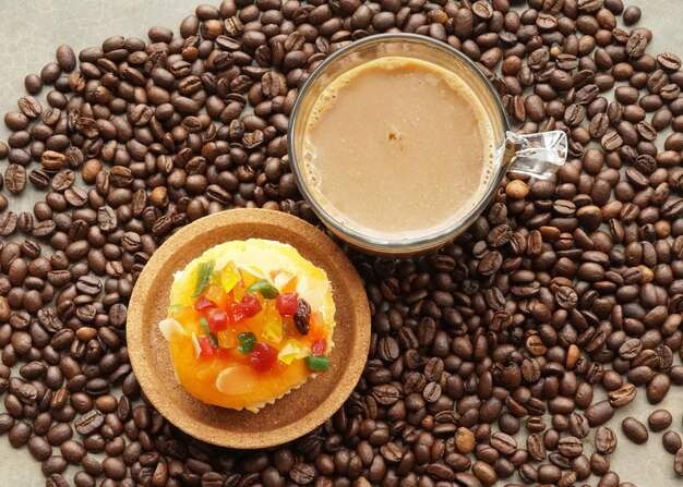 Una taza de café caliente y bizcocho Mixfruit sobre fondo de granos de café