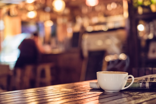 Taza de café caliente del café express con el periódico en el fondo de madera de la falta de definición del bokeh de la iluminación de la tabla