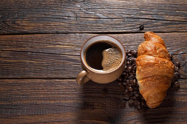 Taza de café caliente y croissant en la mesa de madera oscura Espacio para texto