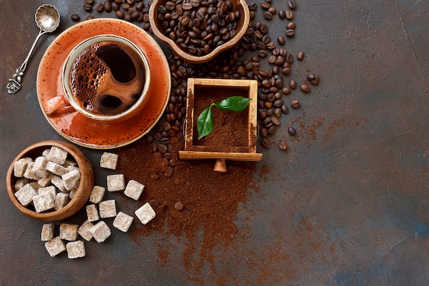 Taza de café caliente, cuchara con aroma de granos de café en un plato y hojas verdes frescas