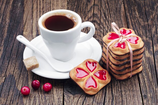 Taza de café caliente y galletas atadas con cinta y arándano en la mesa de madera