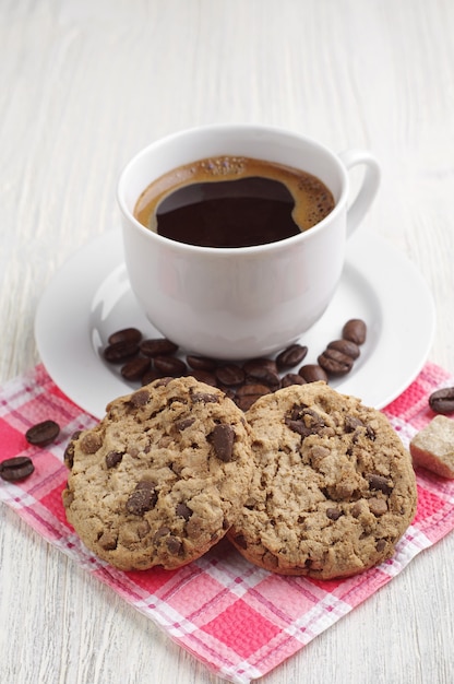 Taza de café caliente con galletas de chocolate en una mesa de madera clara