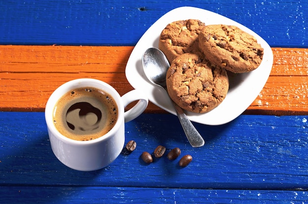 Taza de café caliente con galletas de chocolate en una mesa de madera colorida