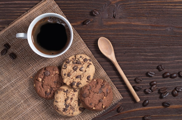 Taza de café caliente y galletas con chocolate y nueces en la mesa de madera marrón, vista superior