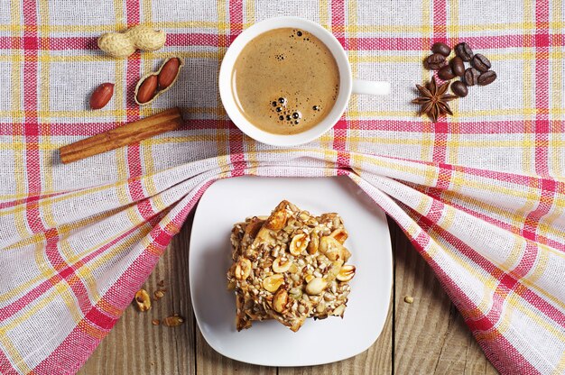 Taza de café caliente y galletas con nueces sobre un mantel cubierto de mesa de madera, vista superior