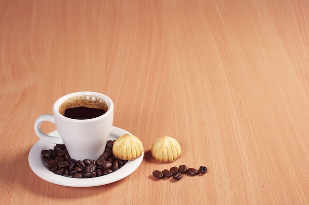 Taza de café caliente y galletas pequeñas en el escritorio