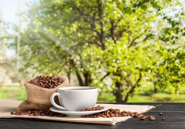 Taza de café caliente con granos de café sobre la mesa de madera y el fondo de las plantaciones