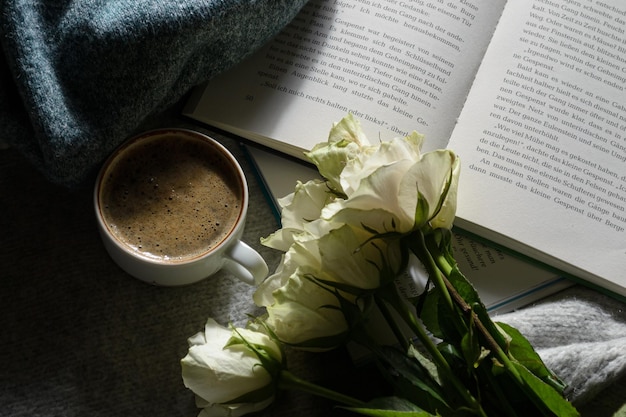 Una taza de café caliente, un libro interesante, un ramo de rosas blancas y un suéter cálido.