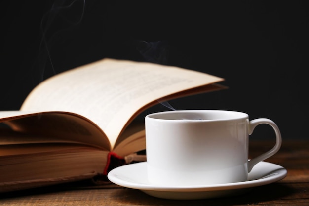 Taza de café caliente con libro sobre la mesa sobre fondo oscuro