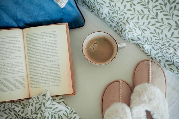 Una taza de café caliente libro zapatillas suaves en la cama desayuno en la cama hogar acogedor.