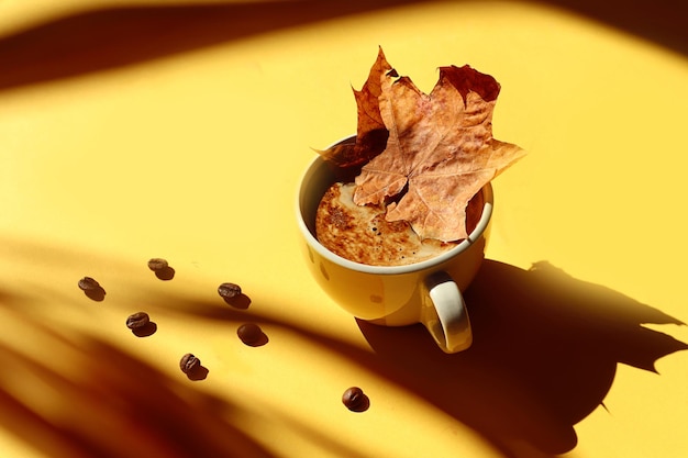 Una taza de café caliente lo calentará en los fríos días de otoño una taza de café amarilla con una hoja de arce en ella granos de café esparcidos sobre un fondo amarillo sombras de objetos