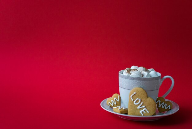 Taza de café caliente con malvaviscos y galletas de corazón con palabras de amor. Mañana del día de San Valentín