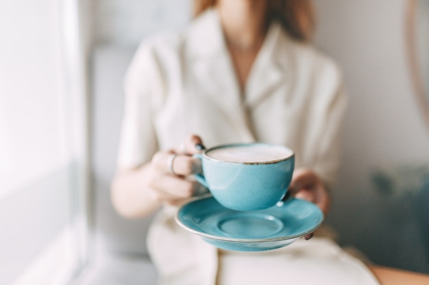 Taza de café caliente en manos de una joven. cafetería atmosférica y platos elegantes.