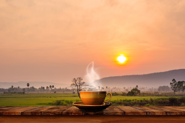 Taza de café caliente en la mesa de madera vieja con el fondo del campo de arroz.