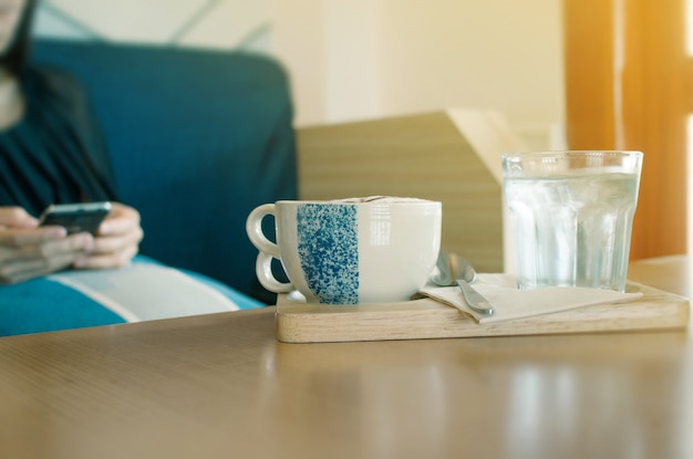 Una taza de café caliente con la mujer borrosa en el fondo.