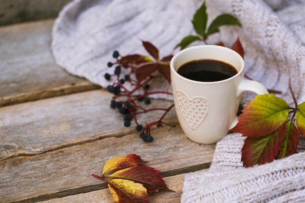 Taza de café caliente en otoño sobre una mesa de madera con una bufanda tejida, suéter