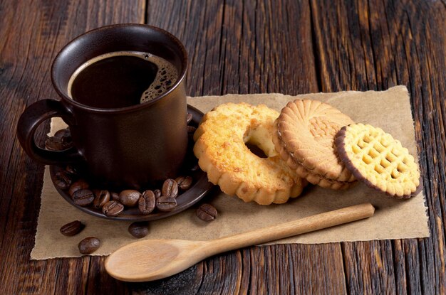 Taza de café caliente y varias galletas dulces en la mesa de madera oscura