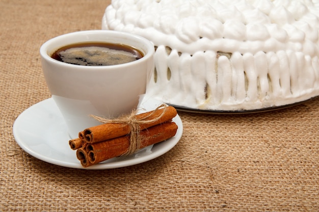 Taza de café, canela y bizcocho decorado con crema batida en mesa con cilicio