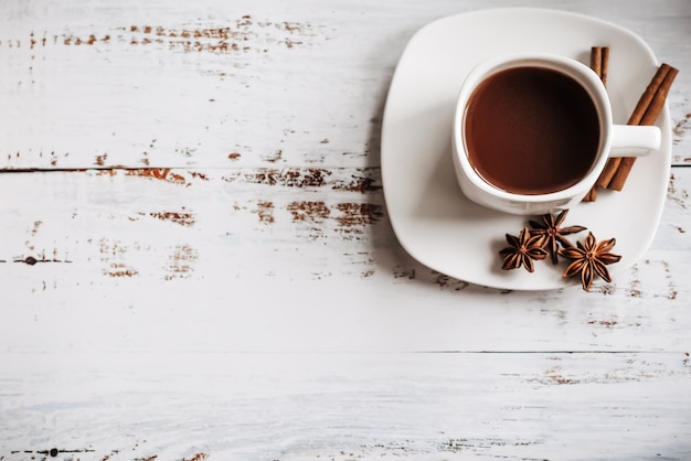 Una taza de café con canela en rama sobre una madera clara