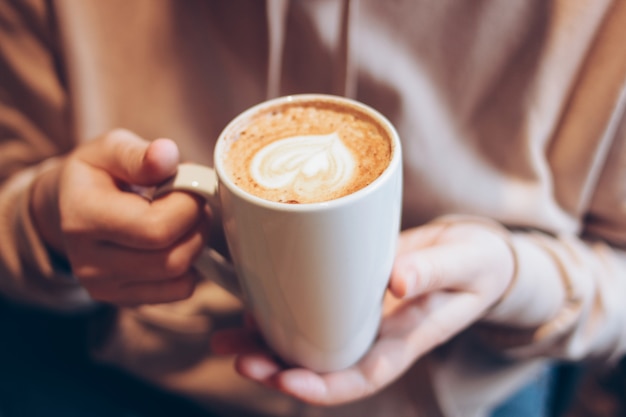 Taza de café cappuccino con corazón de espuma en manos femeninas en el café, de cerca