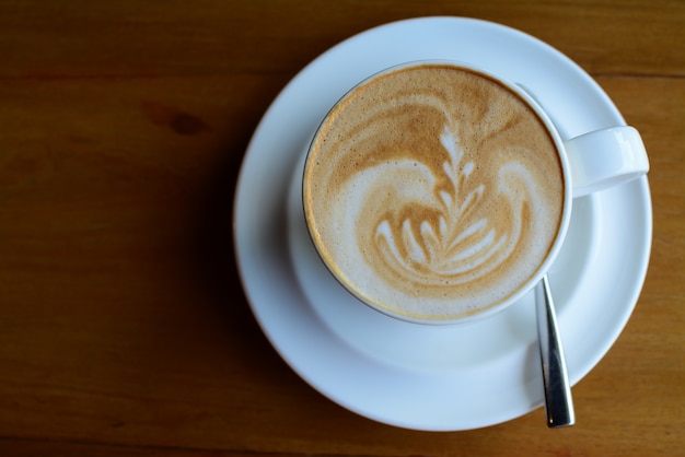 Una taza de café capuchino con arte latte en el fondo de madera sirve en café