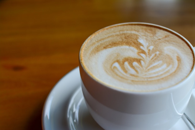 Una taza de café capuchino con arte latte en el fondo de madera sirve en café