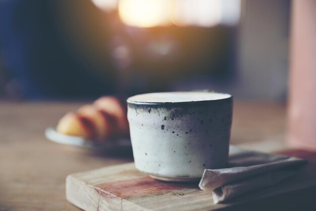 Taza de café capuchino con croissant sobre fondo de madera